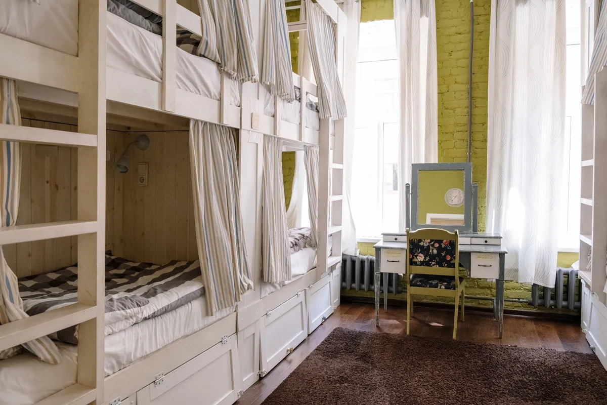A bright dormitory with tiered wooden beds made up in white
